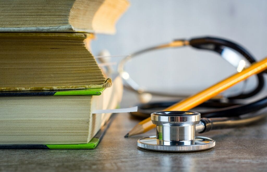 Stacks of medical textbooks beside a stethoscope and pencil, symbolizing the study and practice of healthcare.