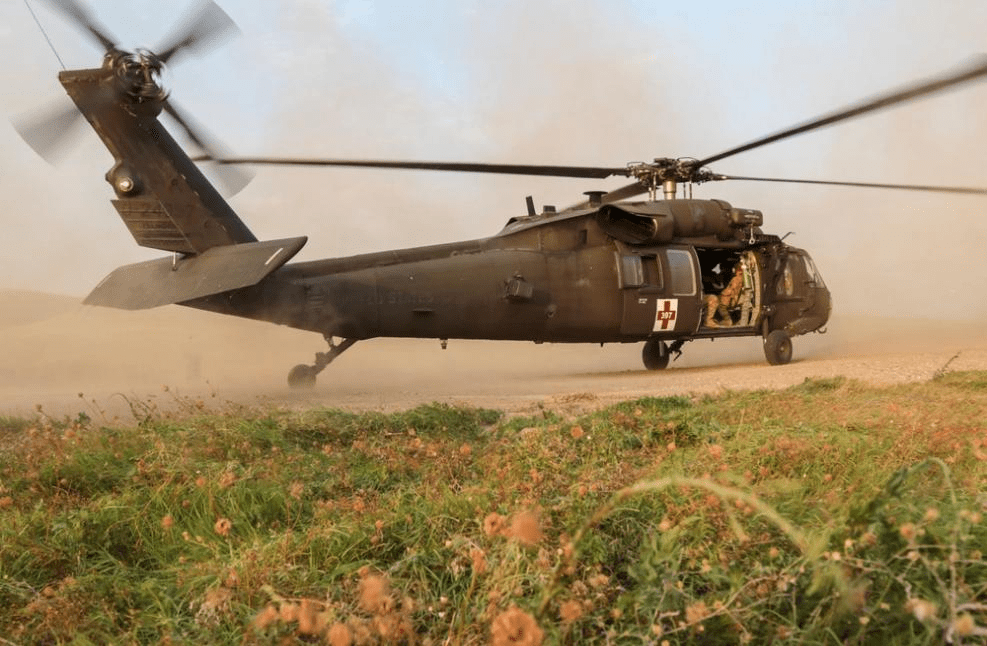 A military helicopter lands on a dusty terrain, revealing soldiers preparing for a mission. The scene emphasizes the operational readiness and environment.
