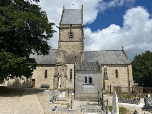 Historic church with a tall stone tower, surrounded by a cemetery in a rural setting under partly cloudy skies.